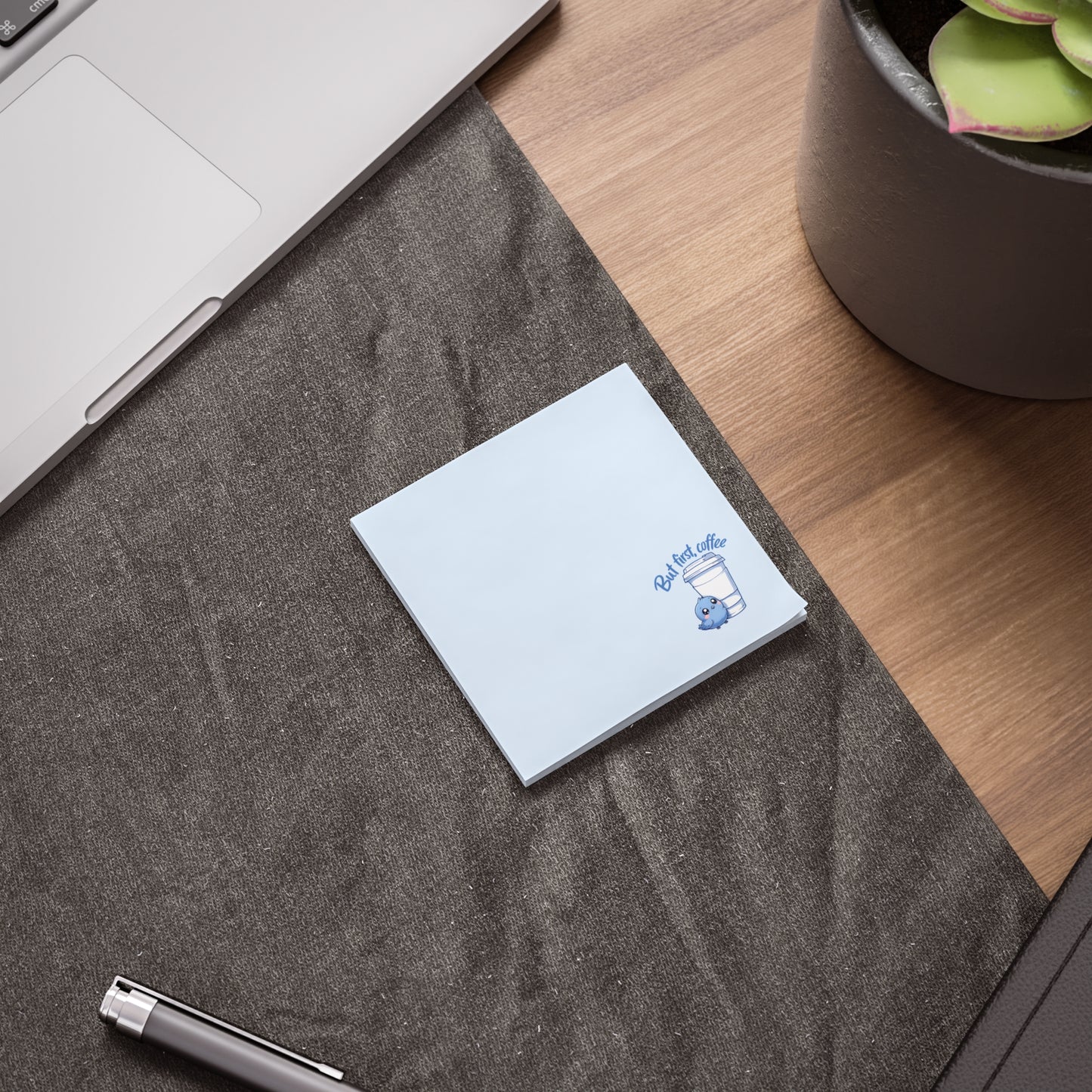 White notebook with a purple logo on a gray surface next to a laptop and plant
