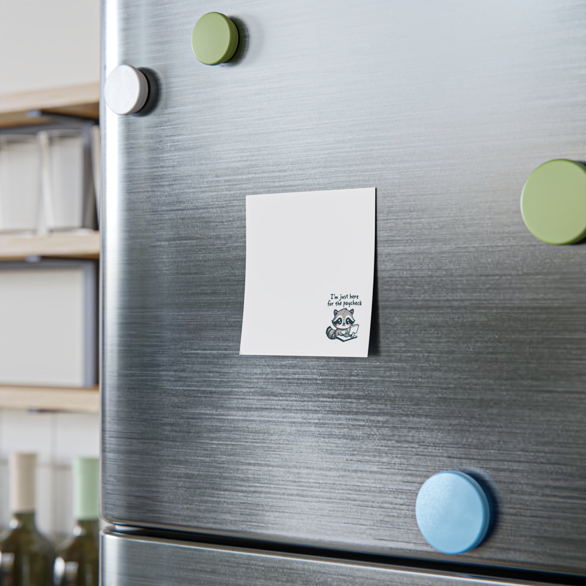 White sticky note with the raccoon illustration and “I’m just here for the paycheck” text at the bottom, attached to a stainless steel refrigerator door with colorful round magnets nearby.