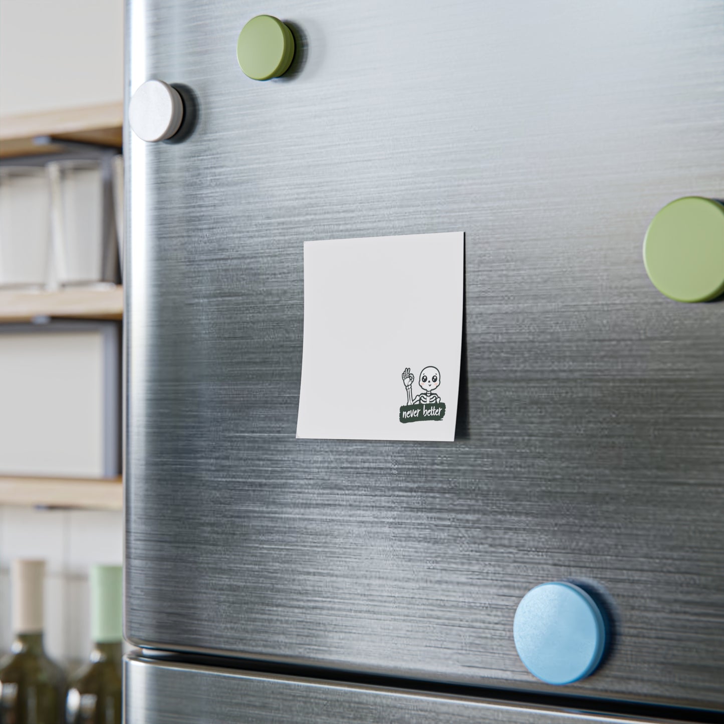 Silver refrigerator with colorful magnets and a white square magnet with a blue circle on a kitchen background.