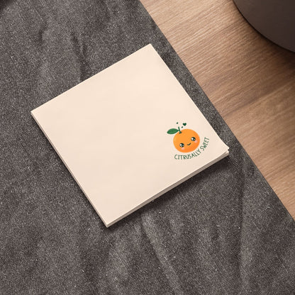 Notebook with a cute orange character on a desk next to a laptop and plant