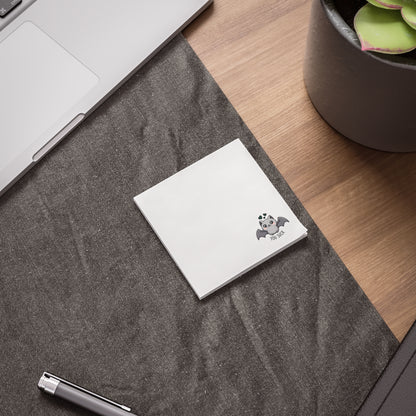 White notebook with a purple logo on a gray surface next to a laptop and plant
