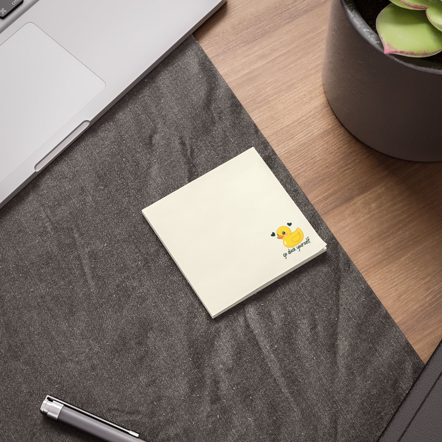 Notebook with a duck illustration on a desk next to a laptop and plant