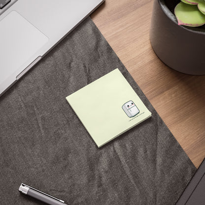 Square sticky note pad on a desk beside a laptop and plant pot, with a small cute fridge illustration in the corner.