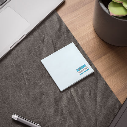 White notebook with a purple logo on a gray surface next to a laptop and plant