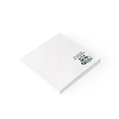 White sticky note pad shown at an angle on a white background, featuring the same raccoon illustration and “I’m just here for the paycheck” text in the bottom right corner.