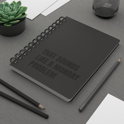 Dark notebook with text on a gray surface with pencils and a plant.